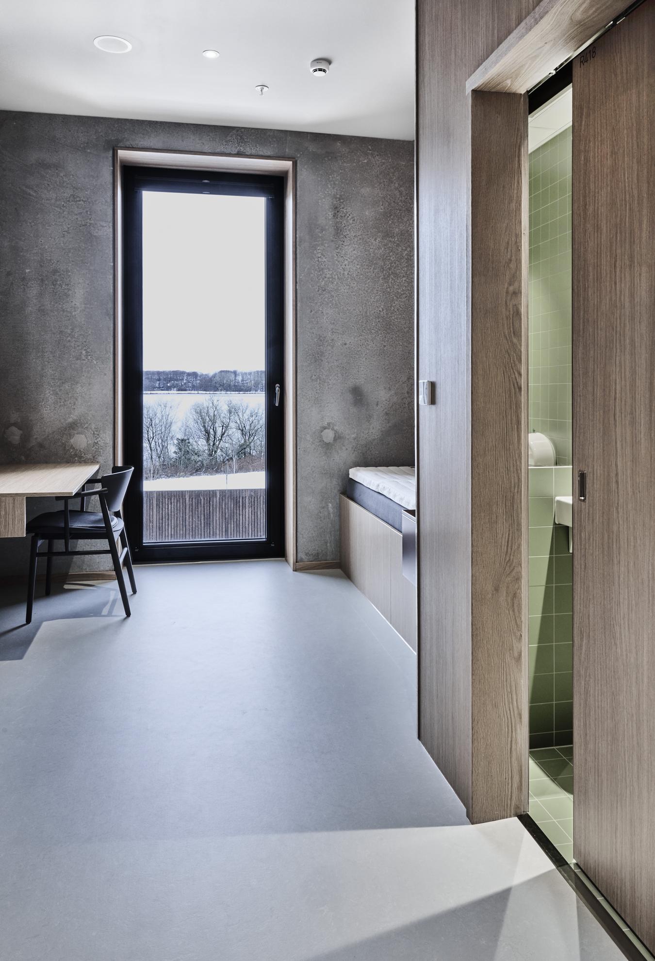 Sovrum och badrum med inredning i betong, trä och grönt kakel. Foto
