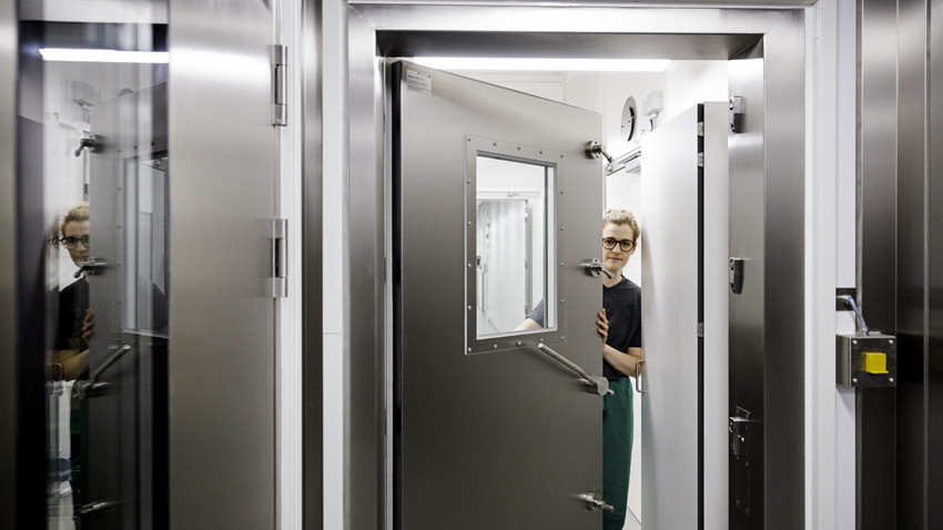 Metalldør som viser hermetisk tett rom for arbeid med smitsomme substanser. Kvinne i døråpning. Foto