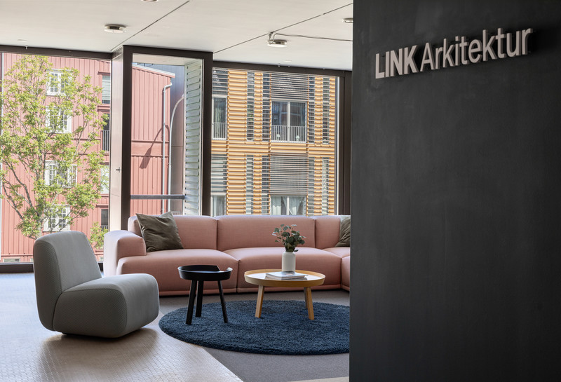 Kontormiljø. Inngangsparti med lounge i rosa og grå. Logo på veggen med LINK Arkitektur. Foto 