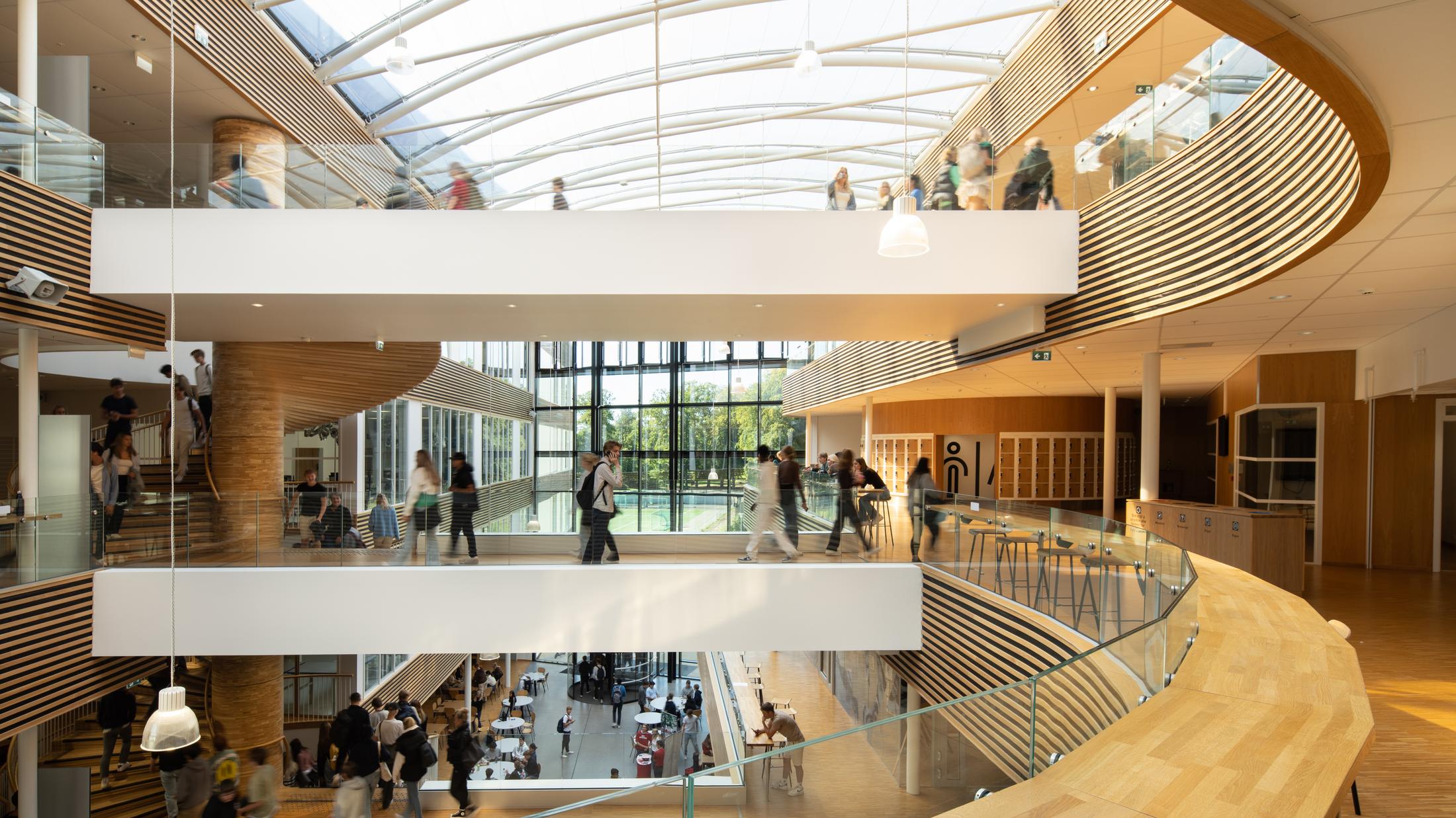 Oversiktsbilde over tre etasjer på skole med treverk og spiler, En trapp i massivtre. Elever i bevegelse. Foto