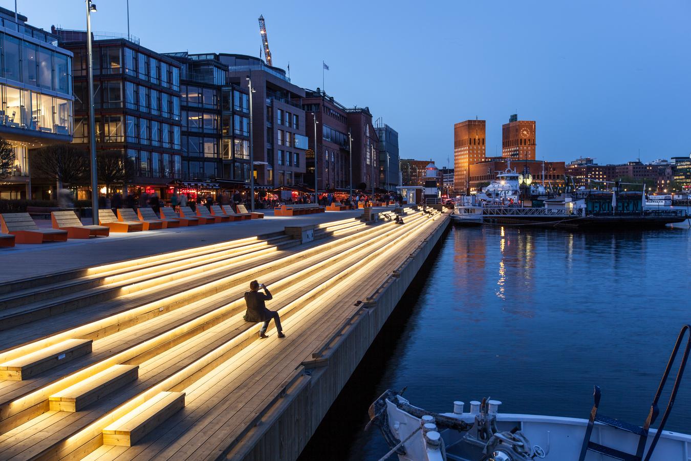 Upplyst bryggae med Oslo Rådhus i bakgrunden. Foto.