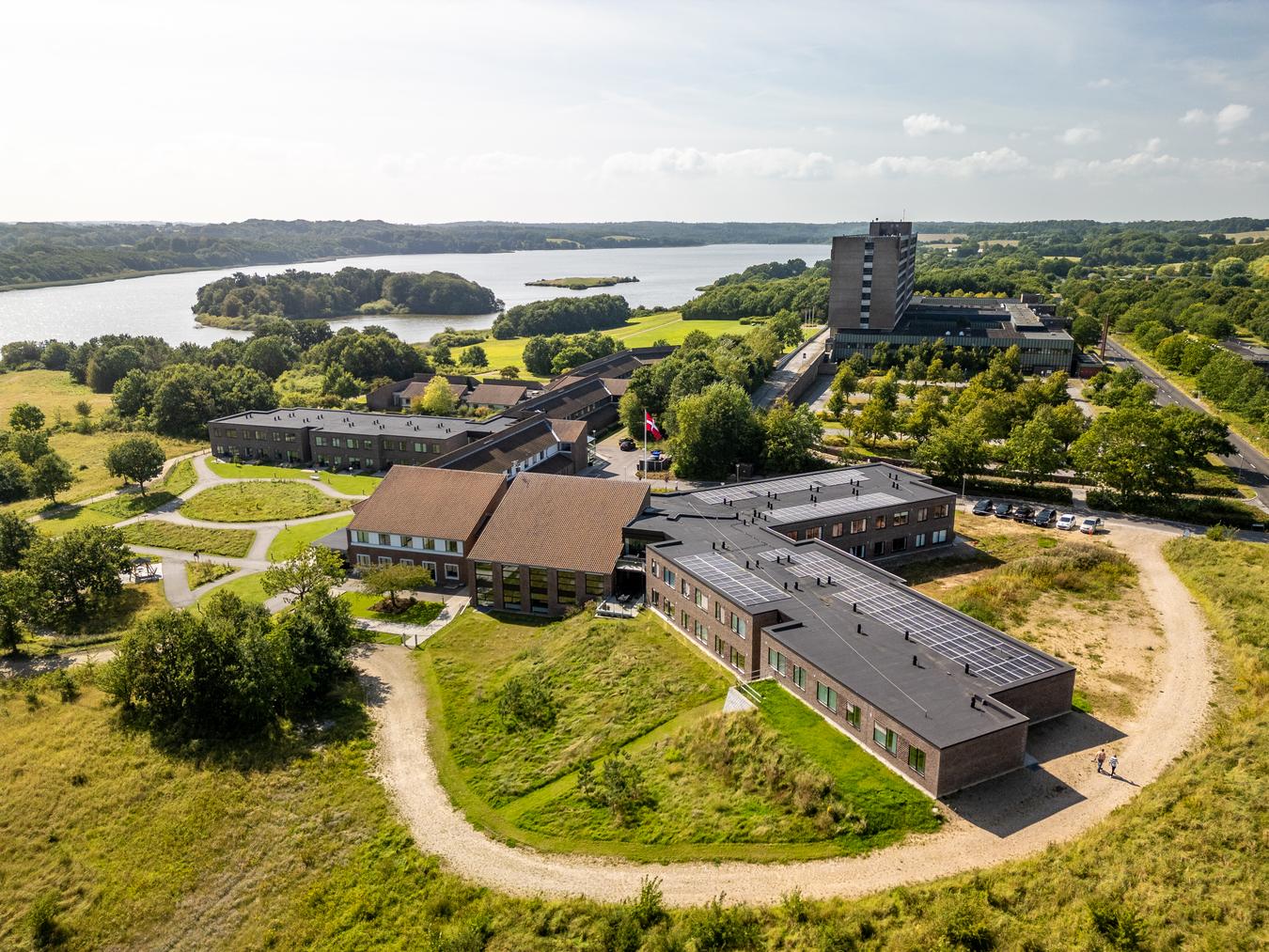 Dronebilde av pleiehjem i grønt skogområde med nærhet til vannet. Foto