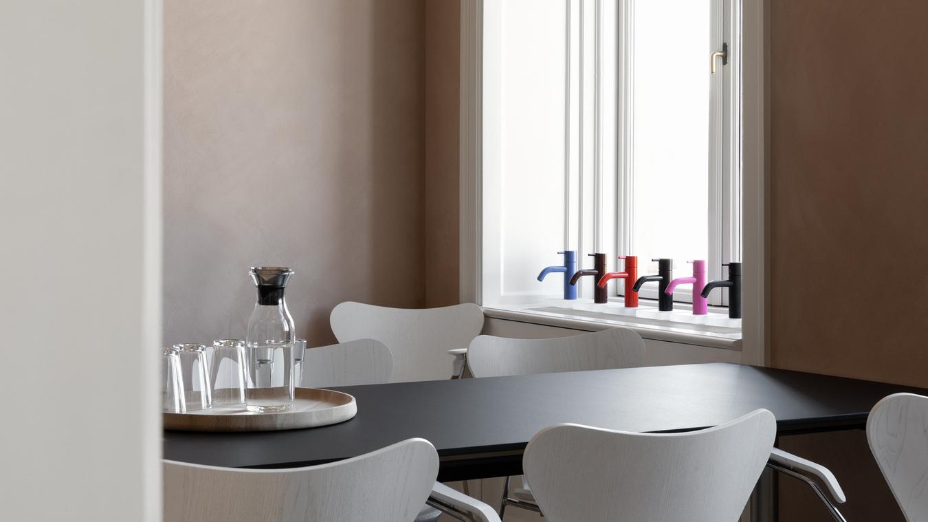 Spisebord og et utvalg fargerike armaturer utstilt i vinduskarmen. Foto